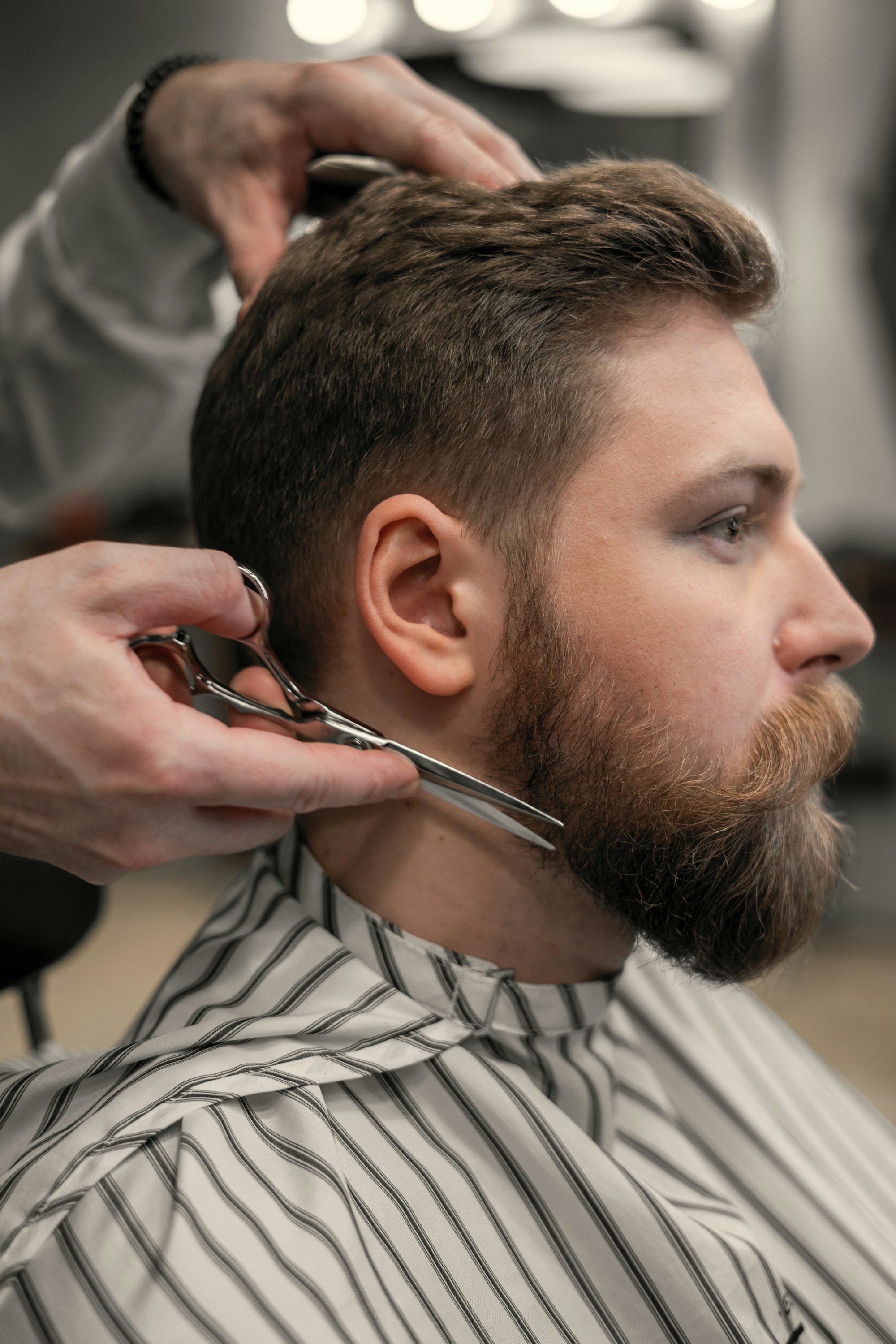 A barber shaping a full beard with scissors